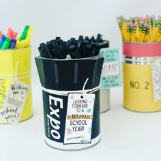 three tin canisters filled with markers and pencils next to each other on a white surface