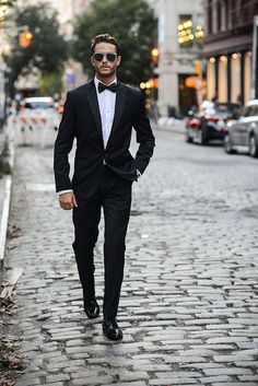 a man in a tuxedo and sunglasses walking down a cobblestone street