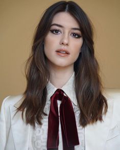 a woman with long hair wearing a white shirt and red tie, looking at the camera