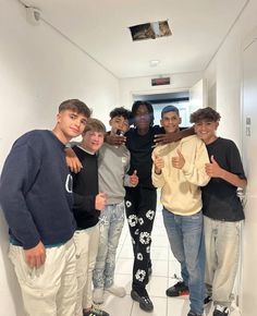 a group of young men standing next to each other in a hallway with white tiles on the floor