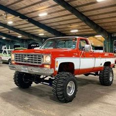 an orange and white truck parked in a garage with big tires on it's tires