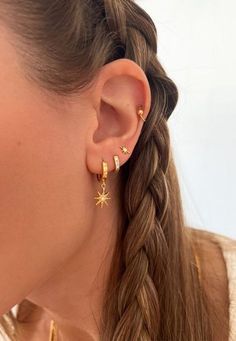 a woman wearing gold earrings with stars on the back of her ear, in front of a white background