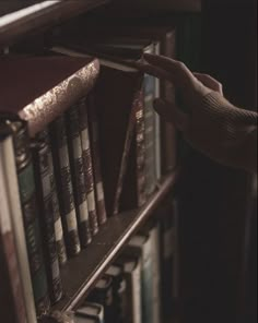 a person reaching for books on a book shelf