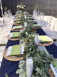 a long table set with place settings and green napkins on it, along with greenery