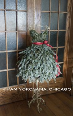 a dress made out of pine branches hanging on a doorknob with a red ribbon