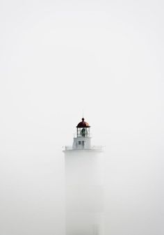 a light house in the fog with an umbrella on it's roof and two people standing at the top