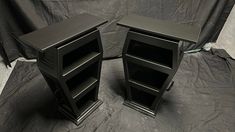 two black shelves sitting on top of a gray cloth covered floor next to each other