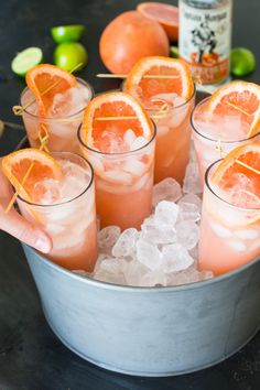 a person holding up some orange slices in a metal bucket with ice and limes around it