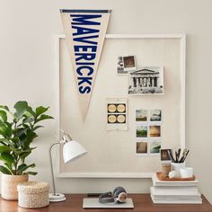 a desk with a white board and some pictures on the wall next to a potted plant