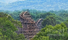 an amusement park roller coaster in the middle of a wooded area with mountains in the background