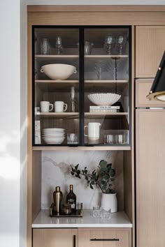 an open cabinet with dishes and cups on the top shelf, in front of a marble countertop