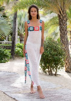 a woman in a white dress is standing on the beach with palm trees behind her