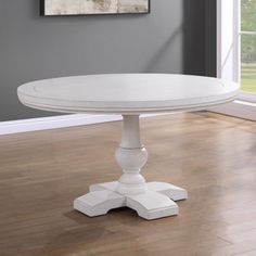 a white dining table in a room with hard wood flooring and large window overlooking the yard