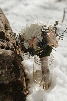 a mason jar filled with flowers sitting on top of snow next to a stone wall