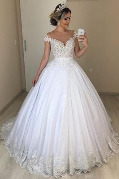 a woman in a white wedding dress taking a selfie with her cell phone while wearing a tiara