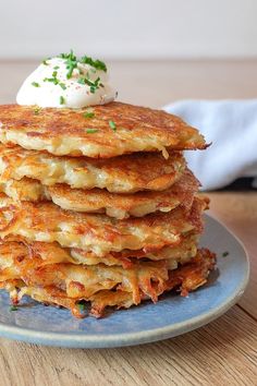 a stack of pancakes on a blue plate topped with whipped cream and chives, sitting on a wooden table