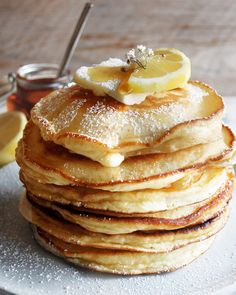 a stack of pancakes with lemon slices and powdered sugar