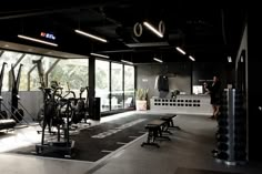 a gym with rows of exercise equipment and people looking out the windows at trees in the distance