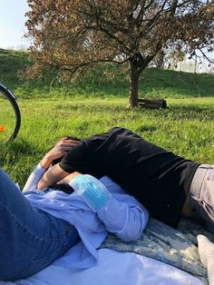 a man laying on top of a blanket next to a tree