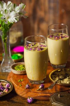 two glasses filled with food sitting on top of a wooden table next to plates and flowers