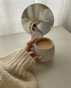 a woman's hand holding a cup of coffee in front of a mirror