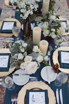 the table is set with blue and white plates, silverware, candles and flowers