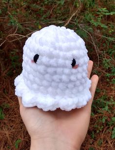 someone is holding up a crocheted white object with black eyes and nose on it