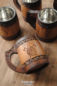 four wooden mugs sitting on top of a table next to metal cups and spoons