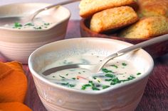 two bowls filled with soup on top of a wooden table next to breadsticks