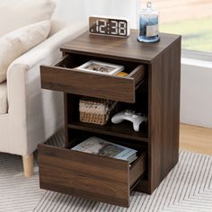 a night stand with two drawers and a clock on the side table next to a couch