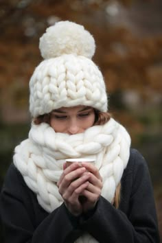 a woman wearing a white knitted hat and scarf holding a cup in her hands