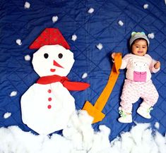 a baby laying next to a snowman on a blue blanket with white snow flakes