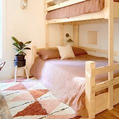 a bunk bed with pink sheets and pillows in a room next to a potted plant