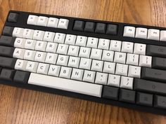 a black and white computer keyboard sitting on top of a wooden table next to a mouse