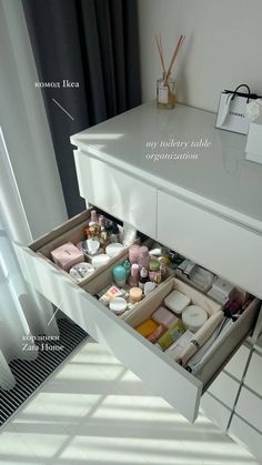 an open drawer in the middle of a white cabinet with lots of items inside it