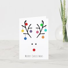 a christmas card with a reindeer's face and colorful balls on its antlers