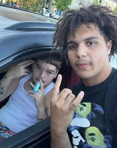 two young men sitting in the back of a car with one pointing at the camera