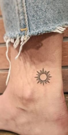 a small sun tattoo on the side of a woman's ankle, with an arrow