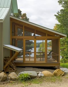 a small cabin with a porch and deck on the side of it, surrounded by rocks