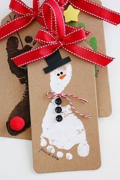 two tags with snowmen on them are tied to brown paper and decorated with red ribbon