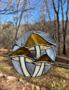 a stained glass sun catcher hanging from a chain in the woods with trees behind it