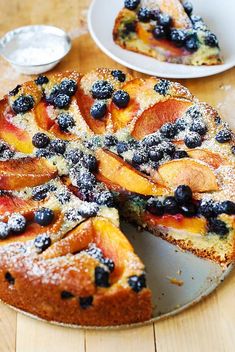 a cake with blueberries and peaches on it sitting on a table next to plates