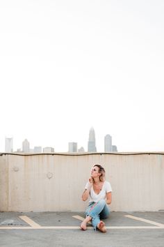 a woman sitting on the ground in front of a wall and talking on her cell phone