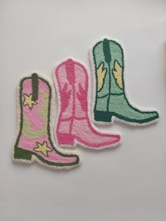 two pairs of pink and green cowboy boots on a white surface, one with yellow stars