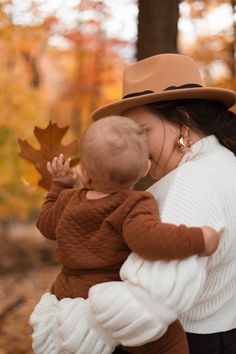 a woman holding a baby in her arms and wearing a hat with leaves on it