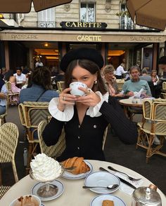 a woman sitting at a table with plates of food and drinks in front of her