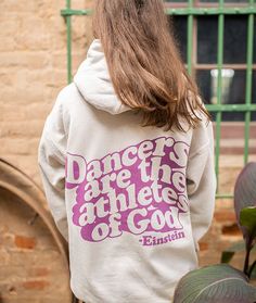 a woman wearing a white sweatshirt with pink lettering on the front and back, standing in front of a brick building