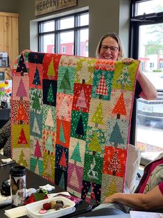 a woman holding up a large quilt in front of a table with plates and cups on it