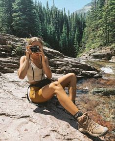 a woman sitting on top of a rock with a camera