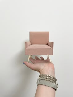 a hand holding a miniature chair on top of a small wooden stick in front of a white wall